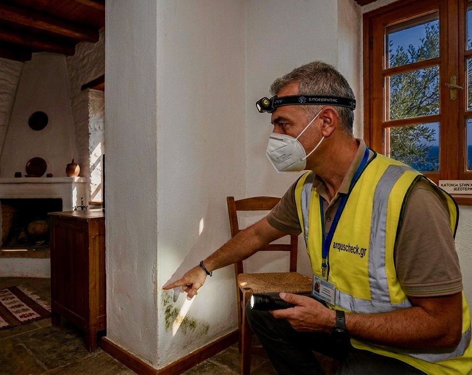 Inspector in PPE pointing to a moisture-damaged wall corner